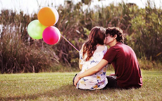 In-love couple kiss sitting on a lawn with balloons